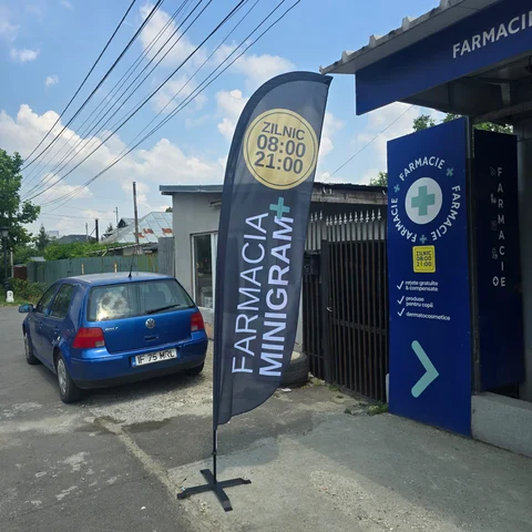 Steag personalizat tip Pana FARMACIA MINIGRAM montat pe suport in fata unei farmacii, cu program ZILNIC 08:00-21:00 — produs de Mora Group, print textil full color pe catarg din fibra de sticla