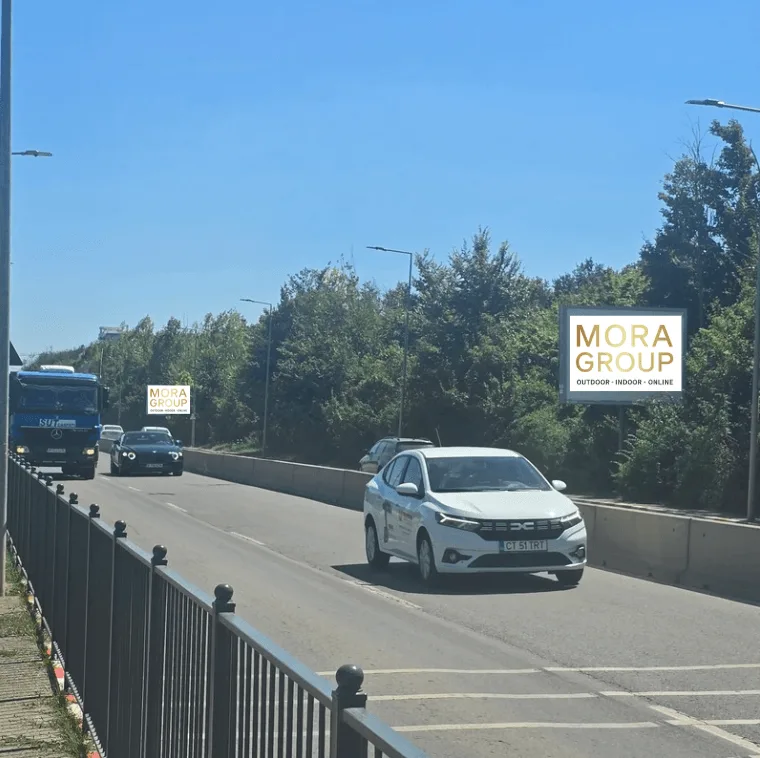 Panou publicitar Mora Group pe strada Erou Iancu Nicolae in Voluntari, Ilfov — billboard alb cu logo gold si text Reclama ta Aici 0756 577 917, vizibil de la artera principala cu trafic rutier intens