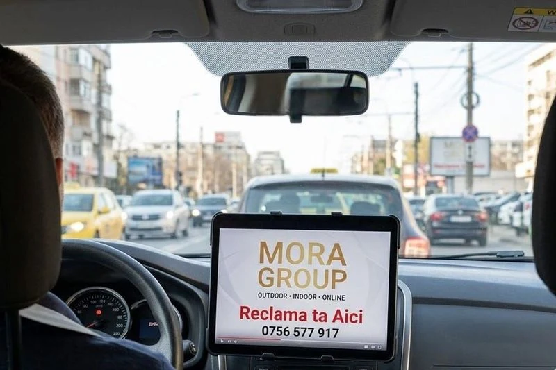 Tableta cu reclama Mora Group montata pe bordul unui taxi din Bucuresti — ecran interior cu spot publicitar pentru pasageri, durata cursa 10-30 minute
