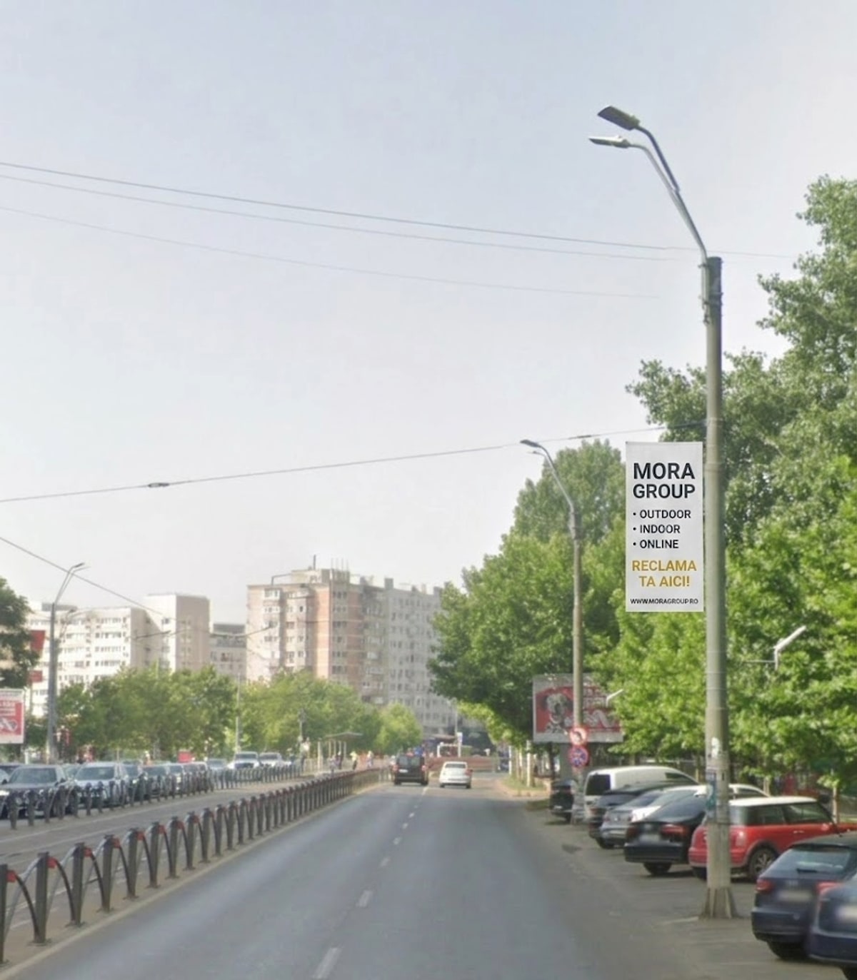 Steag publicitar Mora Group instalat pe stalp de iluminat pe bulevard urban Bucuresti — format 2m × 0,8m vertical, design Outdoor Indoor Online si CTA Reclama ta aici, zona rezidentiala cu trafic auto